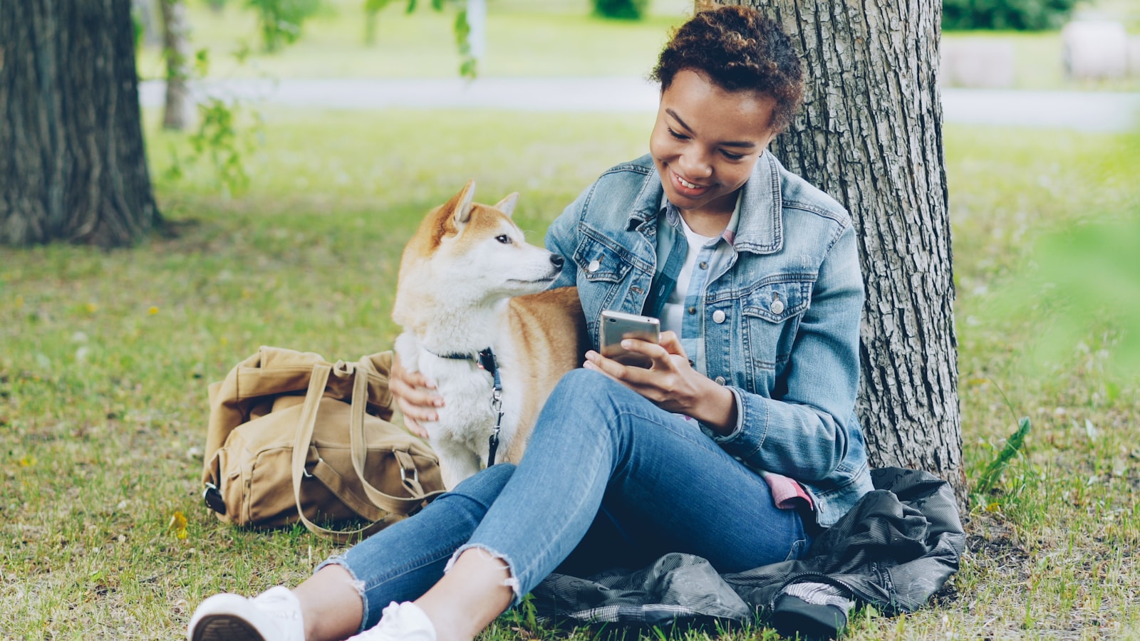 Une femme consulte son téléphone dans un parc, son chien shiba inu à côté d'elle